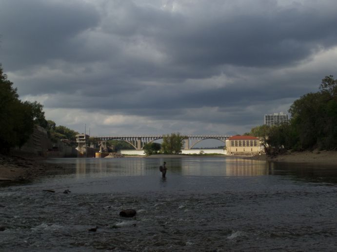 Downstream of a dam in the distance. The sun is setting and a lone fisherman is closer.