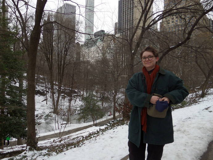 Olivia in snowy central park, skyscrapers in the distance through the trees.