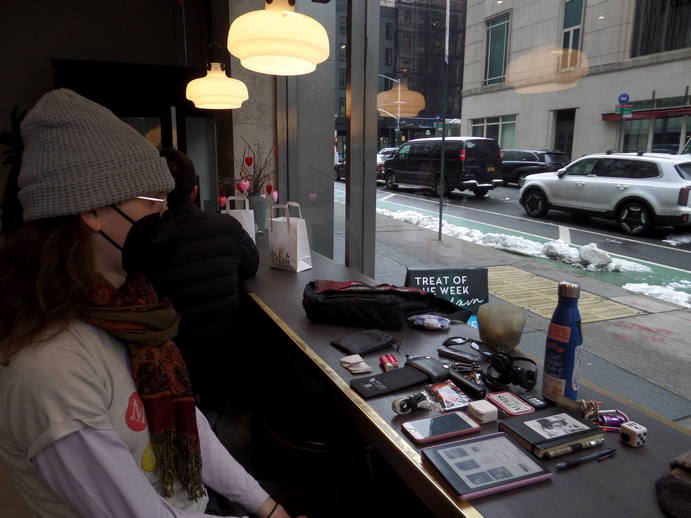 aloe sits masked in a cafe with the contents of her bag on the table.