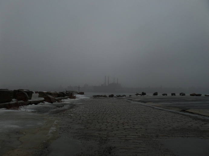 powerplant with smokestacks barely visible through the fog across the water. concrete in the foreground.