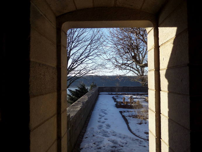 stone square doorway looking out on a snowy garden and bare tree branches.