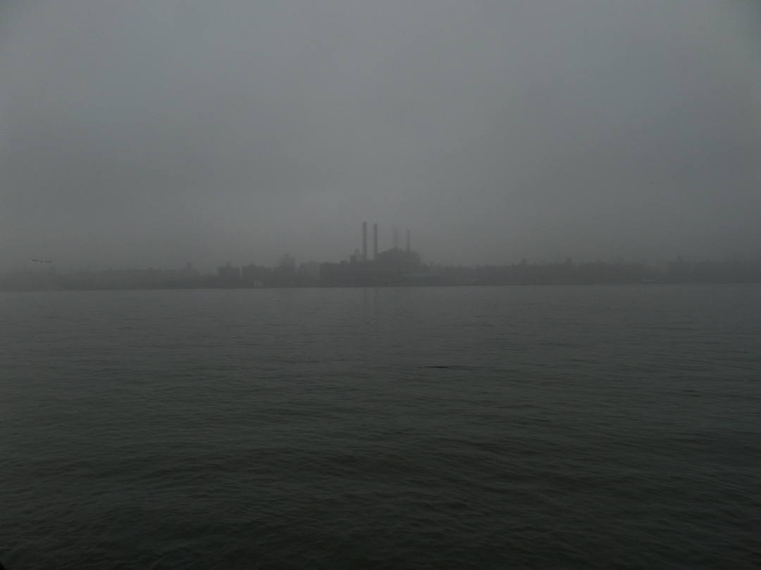 powerplant with smokestacks barely visible through the fog across the water.