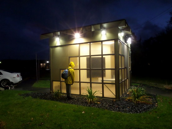 person in yellow raincoat looking into a Bright empty small building; nighttime.