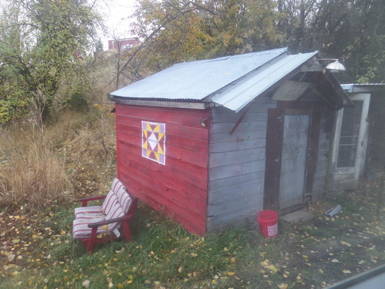 chair in front of a shack with a quilt square painted on the side.